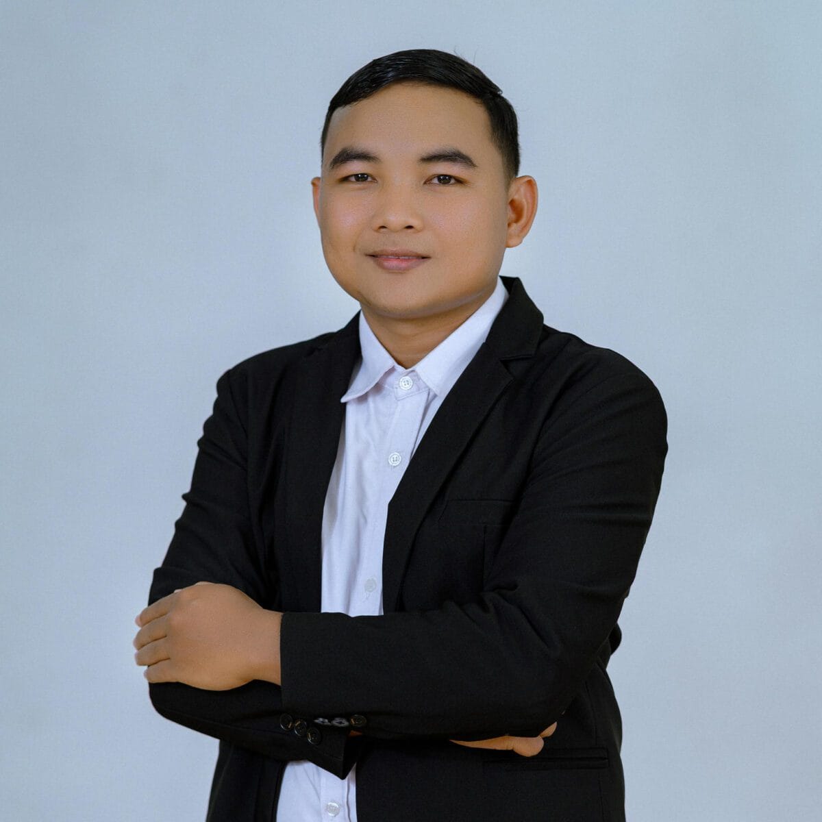 TDSO Young man in formal black suit and white shirt, smiling confidently, standing with arms crossed agai.