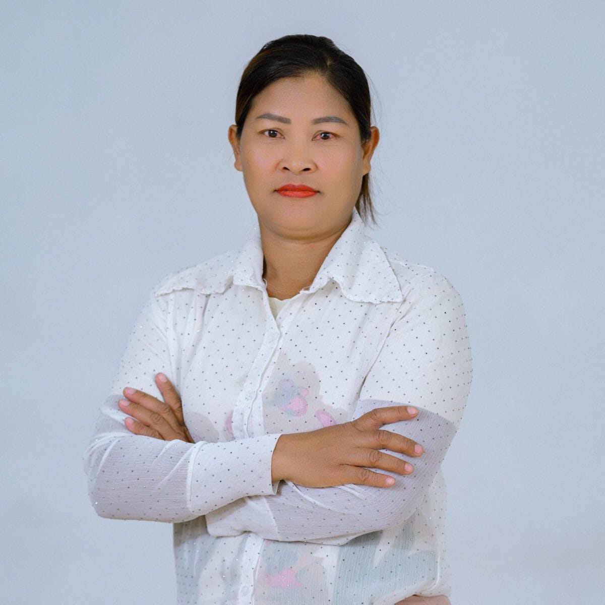 TDSO Empowered woman teacher with crossed arms, confident expression, wearing a white polka dot shirt.
