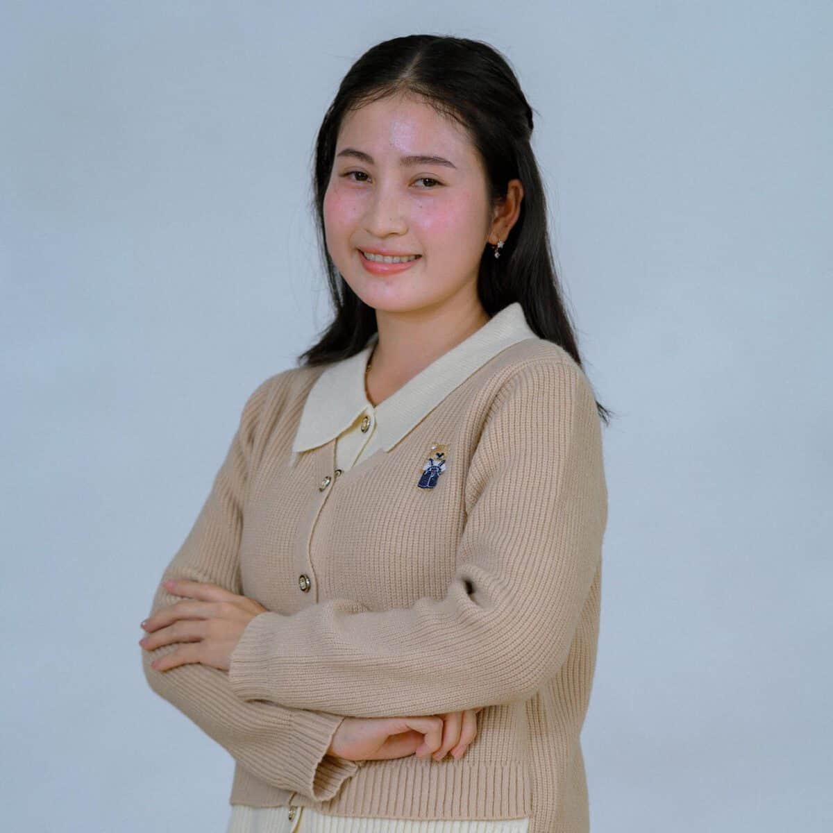 TDSO Female teacher smiling confidently with crossed arms in classroom setting.