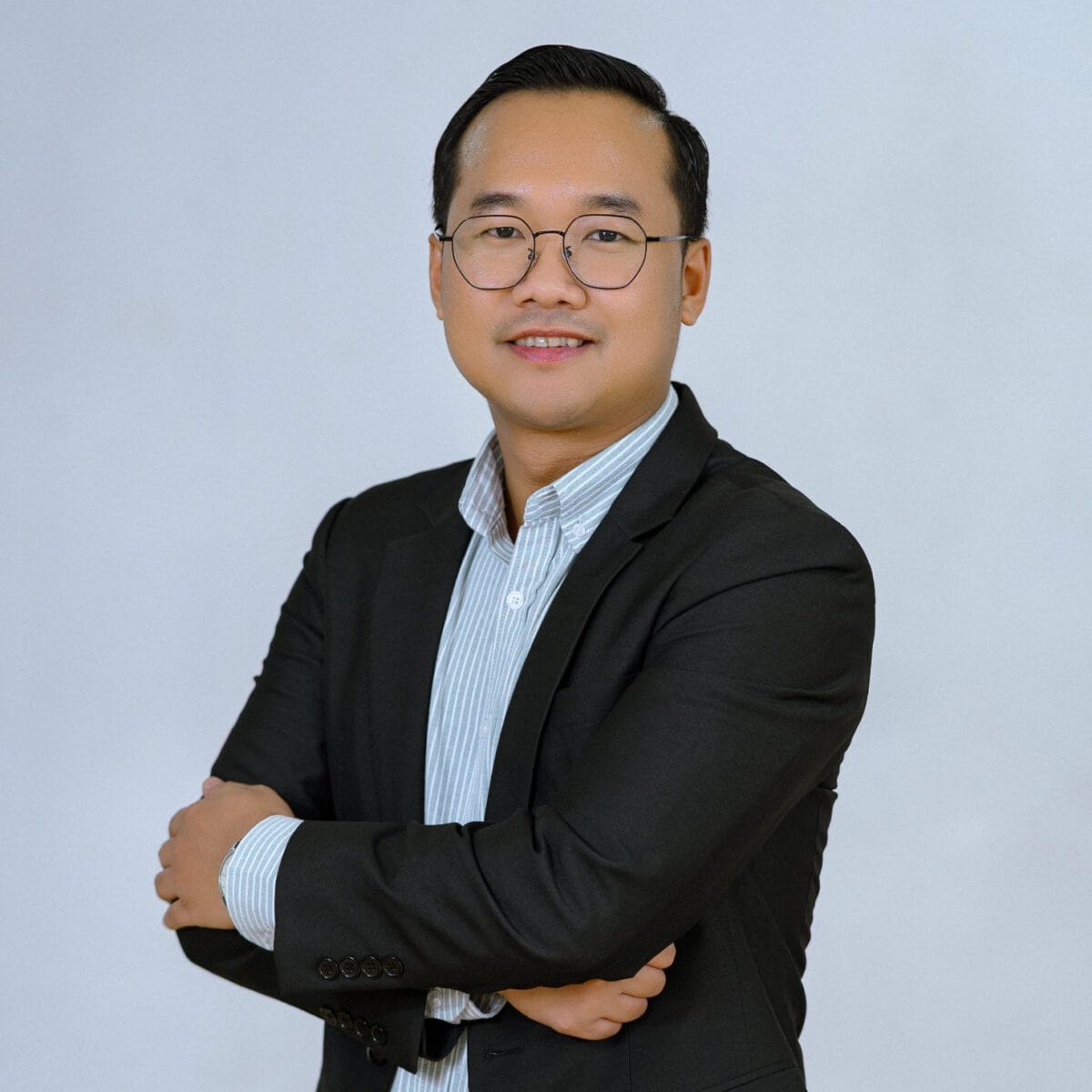 TDSO An Asian male teacher in a black suit and glasses, smiling confidently with arms crossed, representi.