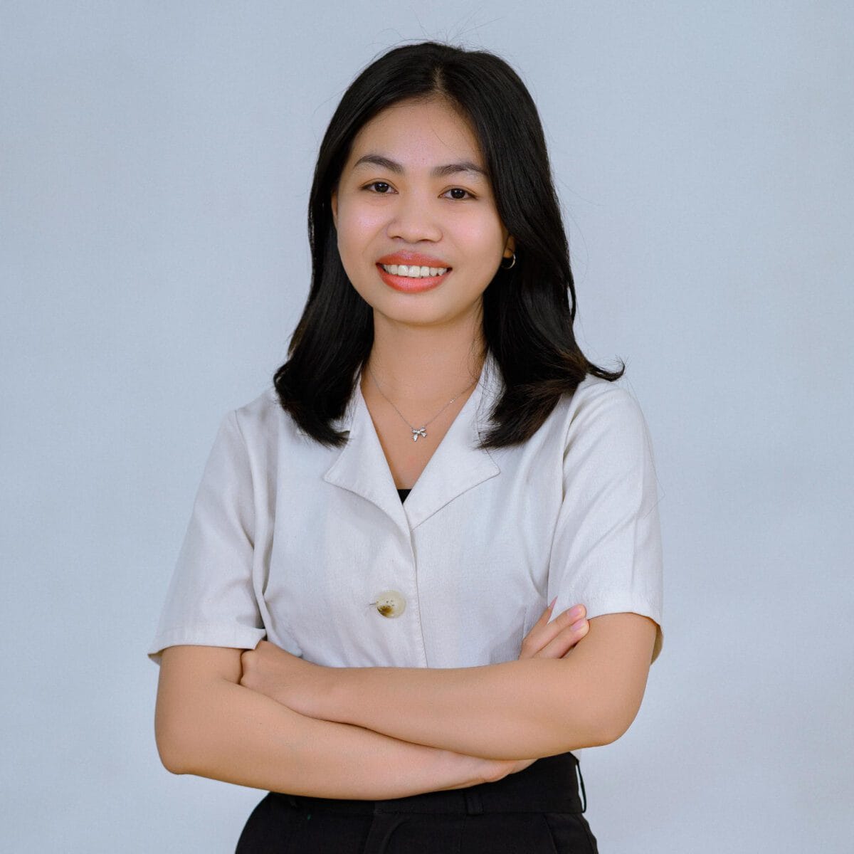 TDSO Female teacher smiling with arms crossed, professional attire, against plain background.